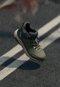 Chaussure de sport verte avec une tige texturée, des accents gris et une semelle de couleur claire. Présente un design à lacets et un bout renforcé.