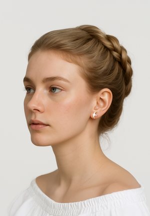 Acconciatura raccolta intrecciata; modella che indossa piccoli orecchini argento a forma di mezzaluna; carnagione chiara; semplice blouse bianca scollata sulle spalle.