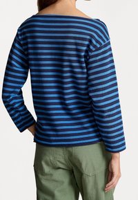 Blå och marinrandig långärmad topp med båthalsringning, med en avslappnad passform och ribbat mönster. Matchad med olivgröna byxor.