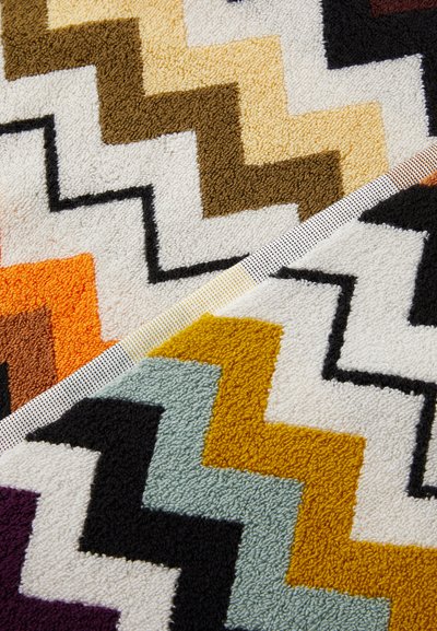 Flerfarget zigzag-mønstret teppe med luksuriøs tekstur, i nyanser av krem, brunt, oransje, petrol og svart i et geometrisk design.
