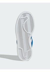 Sapatilha azul com uma sola de borracha branca texturizada apresentando um padrão zig-zag. A parte superior é azul com detalhes brancos.