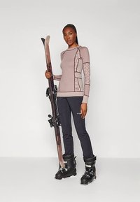 Síkabát, amely egy világos rózsaszín és sötét nadrág mintás, testhez simuló, hosszú ujjú felsőből áll; fekete síbakancsok és sílécek kötésekkel.