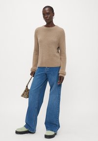 Maglione lavorato a maglia beige con maniche lunghe, abbinato a jeans blu a gamba larga. Accentuato da scarpe verdi chunky e una piccola borsa a stampa zebra.