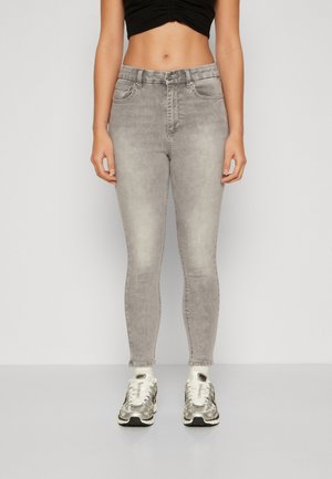 Jean skinny gris avec un délavage, design classique à cinq poches et silhouette ajustée, associés à des baskets à motifs.