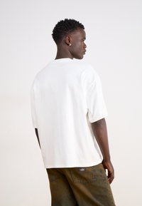 T-shirt bianco in cotone con vestibilità comoda, scollo rotondo e maniche corte, abbinato a pantaloni cargo in denim scuro con un patch del logo.
