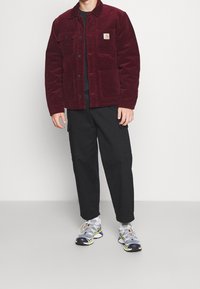Burgundy corduroy jacket with two front pockets, black t-shirt, and black cargo pants. Shoes are gray with yellow and black accents.