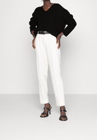 Svart stickad tröja med v-ringning, vita hög midja byxor, svart bälte och svarta klacksandaler med spännen. Enkelt mönster och skräddarsydd passform.