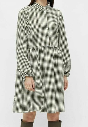 Kobieta ubrana w luźną, czarno-białą sukienkę w kratę gingham z długim rękawem, kołnierzykiem i guzikami z przodu.