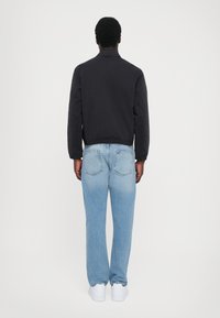 Black bomber jacket, light blue jeans, white sneakers. Jacket features a collar and cuffs; jeans are relaxed fit with back pockets.