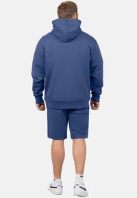 Felpa blu con cappuccio e tasca frontale, abbinata a pantaloni shorts coordinati. Realizzata in tessuto morbido, presenta polsini a costine e una vestibilità comoda.