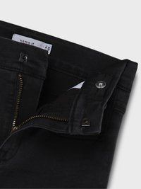 Pantalones de mezclilla negros con cierre de cremallera y botón. Presentan una textura suave y una pequeña etiqueta cosida en el interior de la pretina.