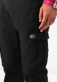 Pantalones cargo negros de algodón con una textura suave, que cuentan con bolsillos laterales, un parche de logo visible y un diseño de corte relajado.