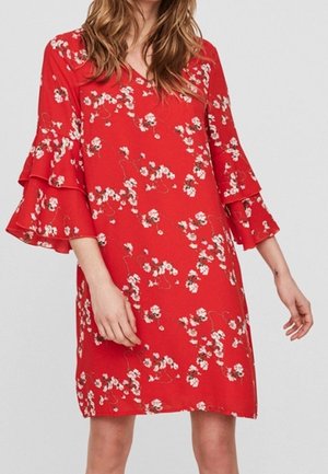 Rotes knielanges Kleid mit weißem Blumenmuster und gestuften Glockenärmeln, getragen von einer Person mit welligem Haar.