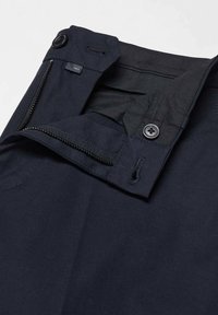 Gros plan sur la ceinture d’un pantalon bleu marine montrant la fermeture éclair, le bouton, la boutonnière et la doublure intérieure en tissu.