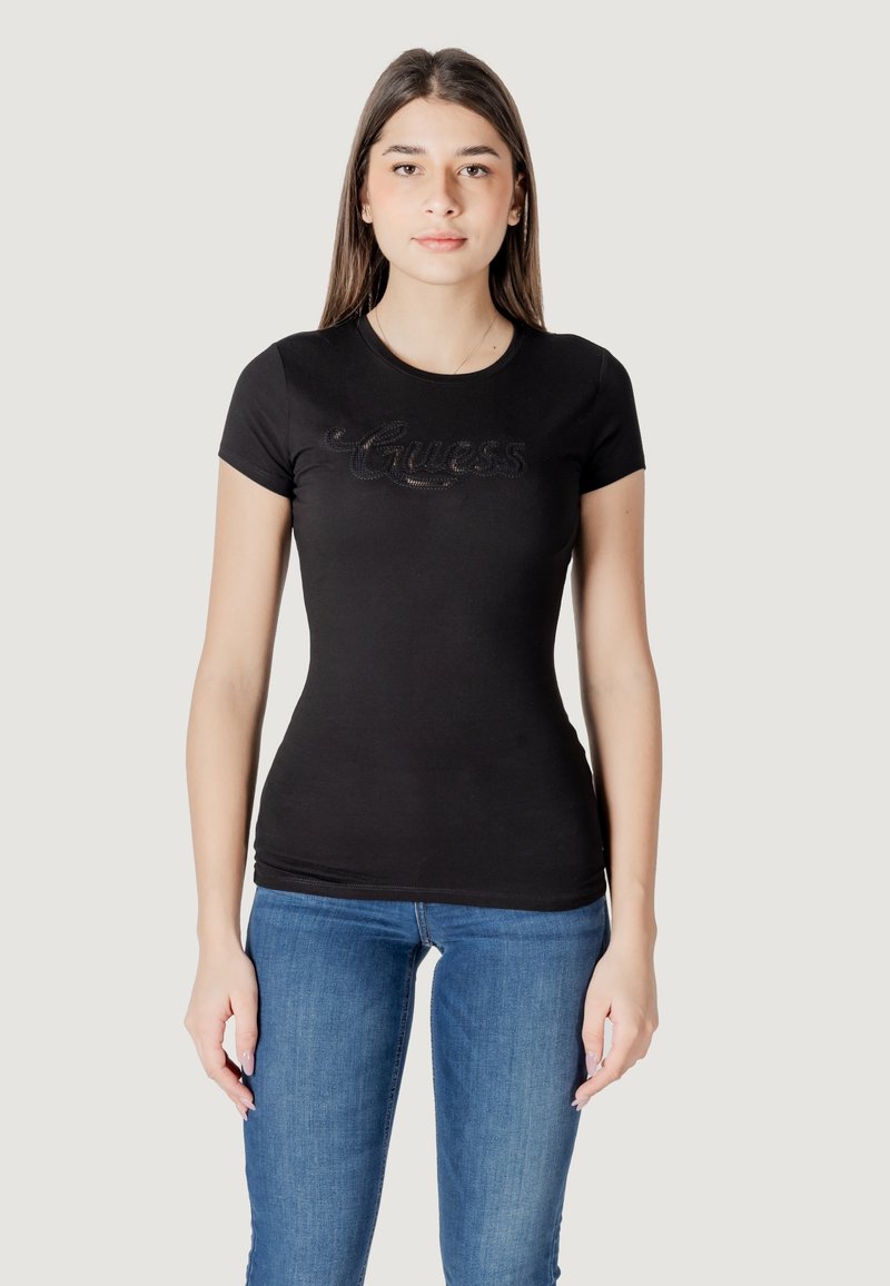 Camiseta negra ajustada de manga corta, con un logo texturizado en el frente. Fabricada con tejido elástico. Combinada con jeans azules.