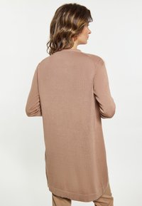 Cardigan cu mâneci lungi, cu model rib pentru un aspect delicat, într-o nuanță moale de bej. Prezintă o croială lejeră, guler rotund și se întinde sub șolduri pentru o acoperire suplimentară.