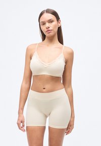 Μπεζ αδιάκοπο σουτιέν με δαντελένιο τελείωμα και ρυθμιζόμενες τιράντες, συνδυασμένο με ταιριαστά σορτς με ψηλή μέση από μαλακό, ελαστικό υλικό.