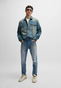 Denim jacket with two chest pockets, faded blue color, and slight wear. Worn with light blue distressed jeans and beige sneakers.
