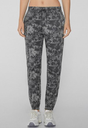 Joggers de patrón negro y gris con cintura ajustable con cordón, corte ajustado y puños elásticos, combinados con zapatillas deportivas de color gris claro.