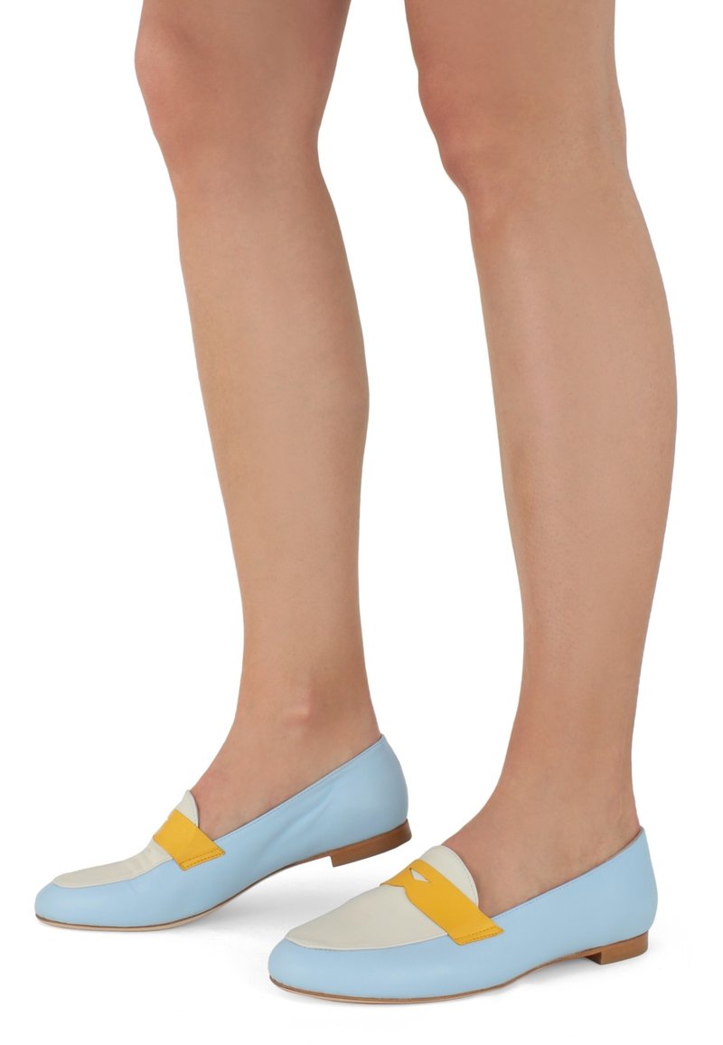 Mocasines de cuero azul claro con una puntera blanca y detalles amarillos. Diseño plano con una textura suave y un estilo minimalista.