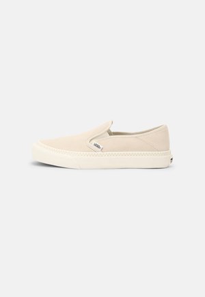 Beżowy but typu slip-on marki Vans z kremową gumową podeszwą i małą naszywką z logo na boku, pokazany z profilu na białym tle.