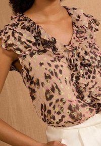 Sheer, light pink blouse with gold leopard spots, ruffled sleeves, and a v-neck design. Smooth texture with a loose fit.