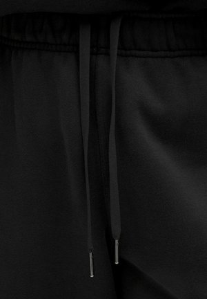 Zwarte sweatpants met een tailleband en trekkoorden, voorzien van metalen aglets die verticaal hangen in het midden.