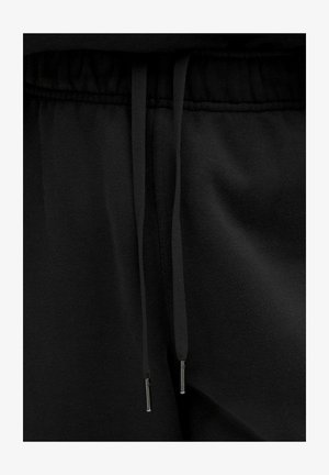 Zwarte sweatpants met een tailleband en trekkoorden, voorzien van metalen aglets die verticaal hangen in het midden.