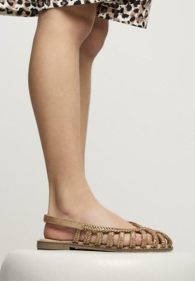 Sandalias trenzadas marrones con punta abierta, que cuentan con un diseño trenzado y una correa en el tobillo. La suela es plana y ligeramente texturizada.