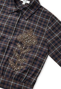 Camicia a quadri marrone con dettagli blu, caratterizzata da ricami floreali con perline e foglie sul lato sinistro. Tessuto morbido, colletto classico.