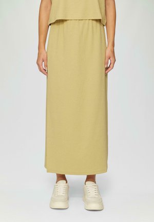 Lange, gele, gestructureerde rok met een elastische tailleband, gecombineerd met lichtgekleurde sneakers. De rok valt tot de enkels.