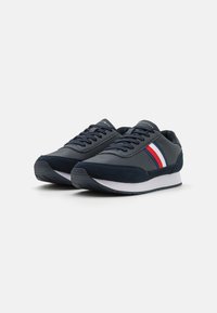 Sneakers blu navy con finitura in pelle liscia e suede. Presentano strisce rosse e bianche sui lati, lacci piatti e una suola in gomma testurizzata.
