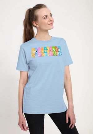 Lysblå bomulds t-shirt med farverige tegneserie-bjørn grafik og teksten "ORIGINAL CARES". Korte ærmer, standard pasform, glat tekstur.