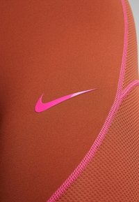 Nike materiał sportowy w kolorze brązowym z różowymi akcentami. Posiada gładką fakturę, przeszywane krawędzie oraz wyróżniające się różowe logo.
