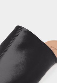 Κοντινό πλάνο μαύρου δερμάτινου επάνω μέρους παπουτσιού με ορατές ραφές και ταμπά εσωτερική σόλα με μερική επωνυμία σε λευκό φόντο.