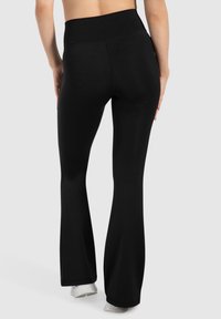 Zwarte uitlopende yogabroekjes met een gladde textuur, hoge tailleband en enkel-lange snit, ontworpen voor comfort en flexibiliteit in beweging.
