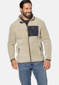 Beige fleece jacket with a black zippered chest pocket, front zip closure, and contrasting black trim along cuffs and hem. Texture is soft.