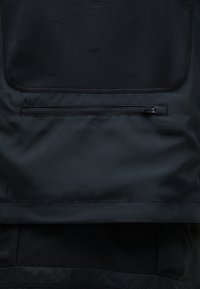 Gros plan d'une surface en tissu noir avec une poche horizontale zippée et un panneau en maille au-dessus.