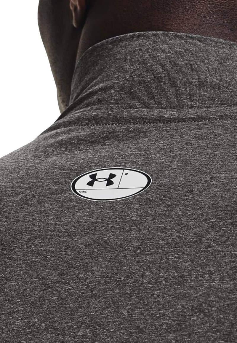 Polo shirt en tissu texturé gris avec un col montant et une étiquette blanche ronde comportant le logo Under Armour au dos.