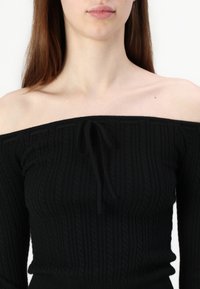 Top preto de ombro a descoberto feito de tecido de malha canelada, com um detalhe de cordão na frente e uma silhueta ajustada.