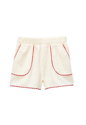 Shorts en tissu texturé couleur crème avec taille élastique et bordure rouge festonnée le long des grandes poches avant et de l'ourlet.