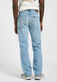 Jeans in denim azzurro chiaro con taglio dritto, cinque tasche e un'etichetta in pelle con logo sulla cintura posteriore. Dettagli di cucitura classici.