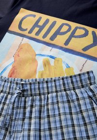 Illustration d'une assiette de fish and chips avec le mot "CHIPPY" au-dessus sur un fond noir, accompagnée d'un tissu à carreaux bleu et noir.