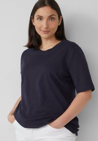 Marineblaues T-Shirt mit kurzen Ärmeln und Rundhalsausschnitt, aus weichem Stoff gefertigt. Bietet eine lockere Passform und glatte Textur, kombiniert mit weißen Hosen.