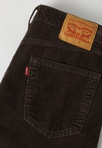 Σκούρο καφέ παντελόνι Levi's από κορντόρι, που δείχνει πίσω τσέπη και καφέ δερμάτινο λογότυπο με κόκκινη ετικέτα Levi's σε λευκό φόντο.
