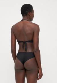 Crni bikini set koji sadrži gornji deo sa vezanjem na leđima i donji deo viskog struka. Glatka tekstura s minimalističkim dizajnom, bez uzoraka ili dodataka.