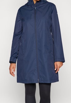 Frau trägt einen navyblauen, knielangen Regenmantel mit Kapuze, Frontreißverschluss und Seitentaschen, kombiniert mit schwarzen Leggings.