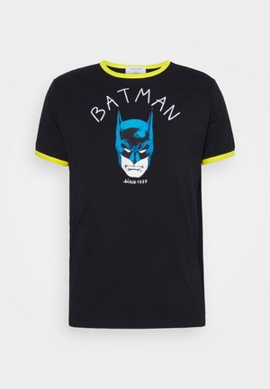 Czarny t-shirt z krótkim rękawem, żółtym obszyciem i niebieską grafiką twarzy Batmana z napisem "BATMAN" oraz "since 1939" na przodzie.