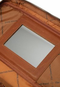 Interior de cuero marrón con un corte rectangular para el espejo, que presenta una marca impresa. Cierre de cremallera a lo largo del borde con costuras en contraste.
