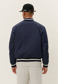 Navy striped bomber jacket with ribbed cuffs and hem, featuring a contrasting band at the collar. Smooth material with a quilted texture.